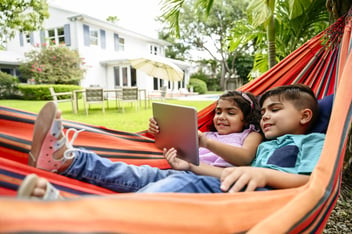 Young siblings using digital tablet in hammock