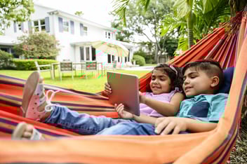 Young siblings using digital tablet in hammock